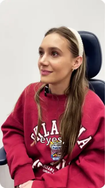 Woman in a red Oklahoma sweatshirt sits and smiles, looking upward.