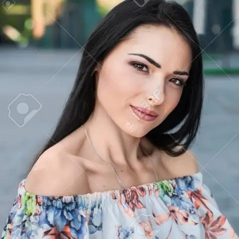 Woman with long dark hair in a floral off-shoulder top smiling gently.