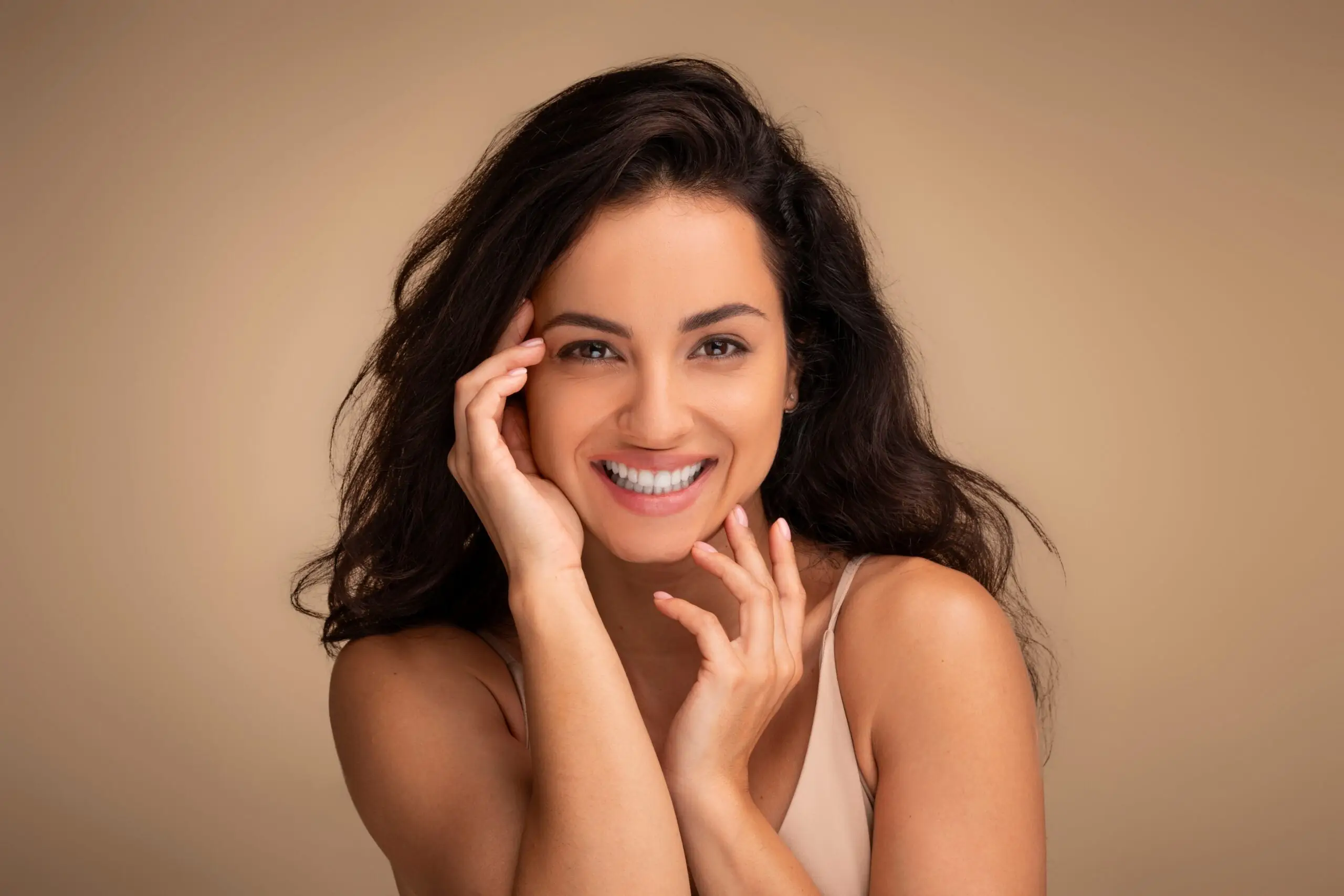 Smiling woman with long dark hair shows chin augmentation results against beige background.