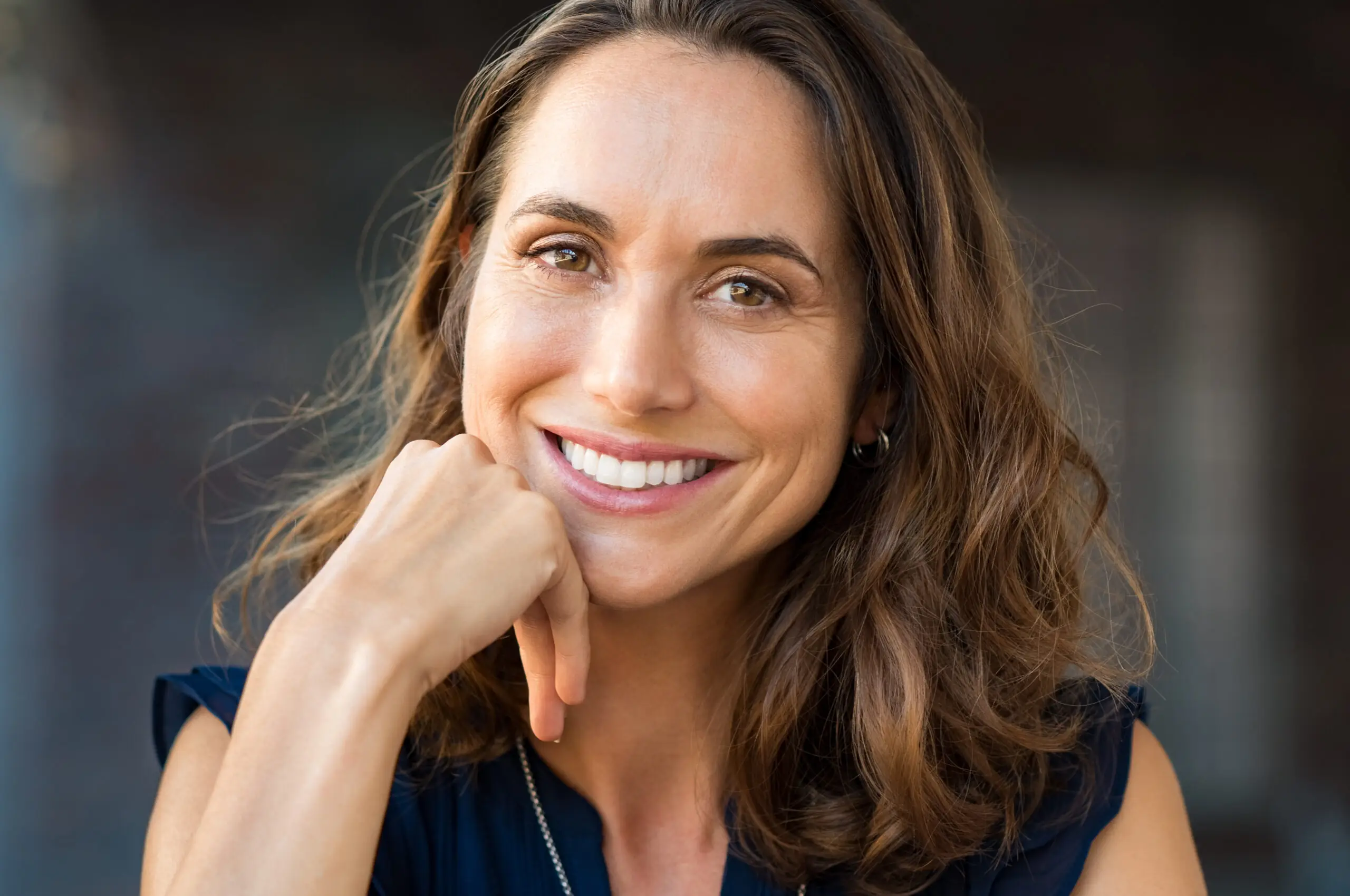 Smiling woman with brown hair rests chin on hand, showing natural results.