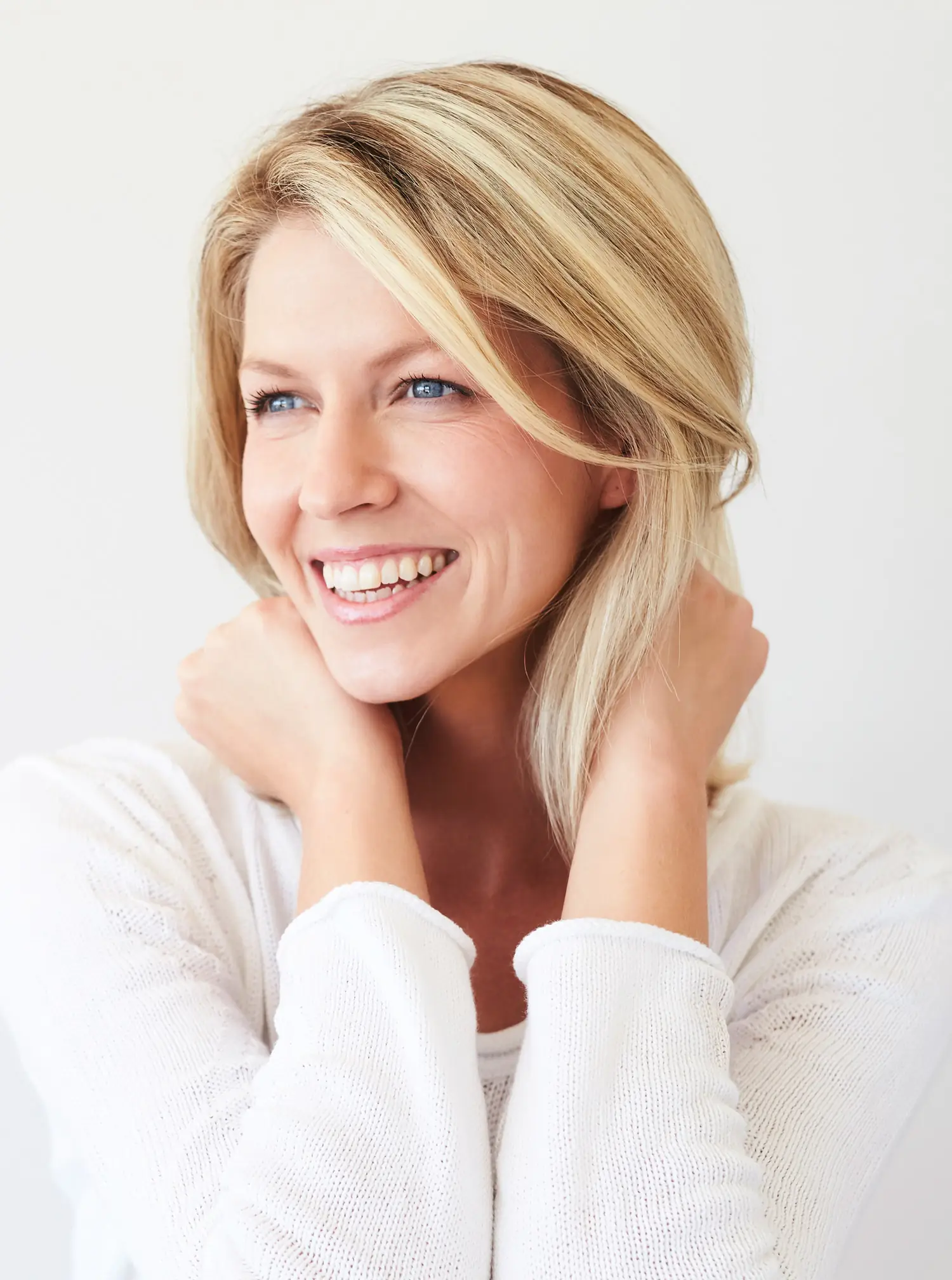 Smiling blonde woman in white top looking sideways after eyelid surgery.